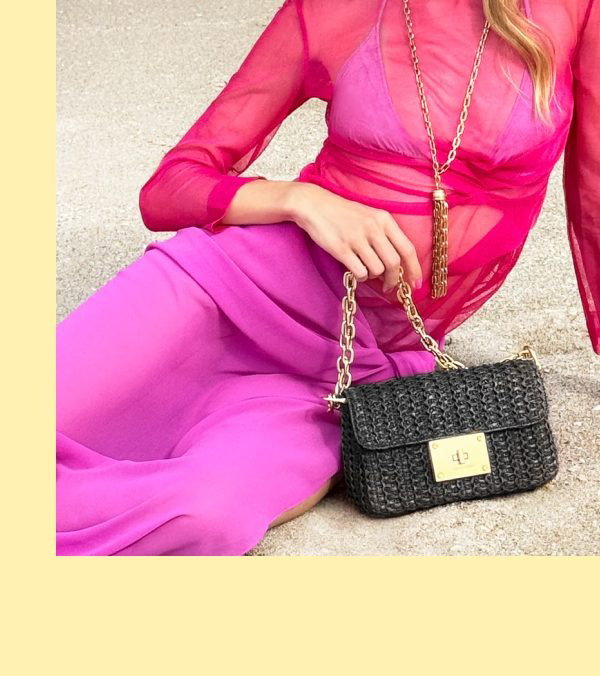A person wearing a pink outfit holds a black handbag, with a light background.
