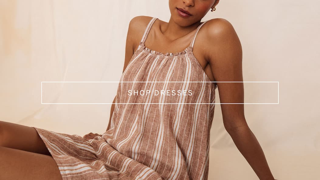 Model reclining in a striped sleeveless summer dress, with overlay text reading “Shop Dresses.”