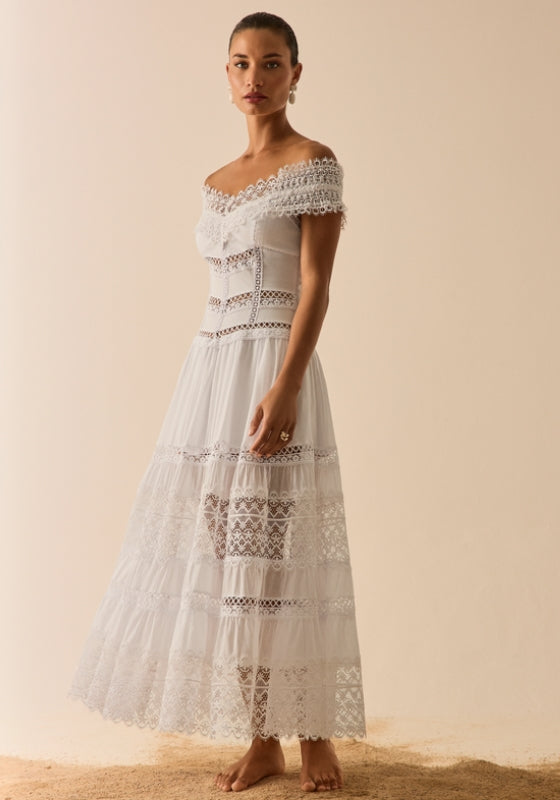 Woman in a pink dress with lace trim stands by the ocean.