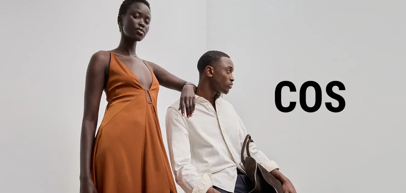 Largo vestido naranja con escote pronunciado y abertura lateral, combinado con una camisa ligera texturizada y pantalones oscuros, acentuado con un bolso marrón.