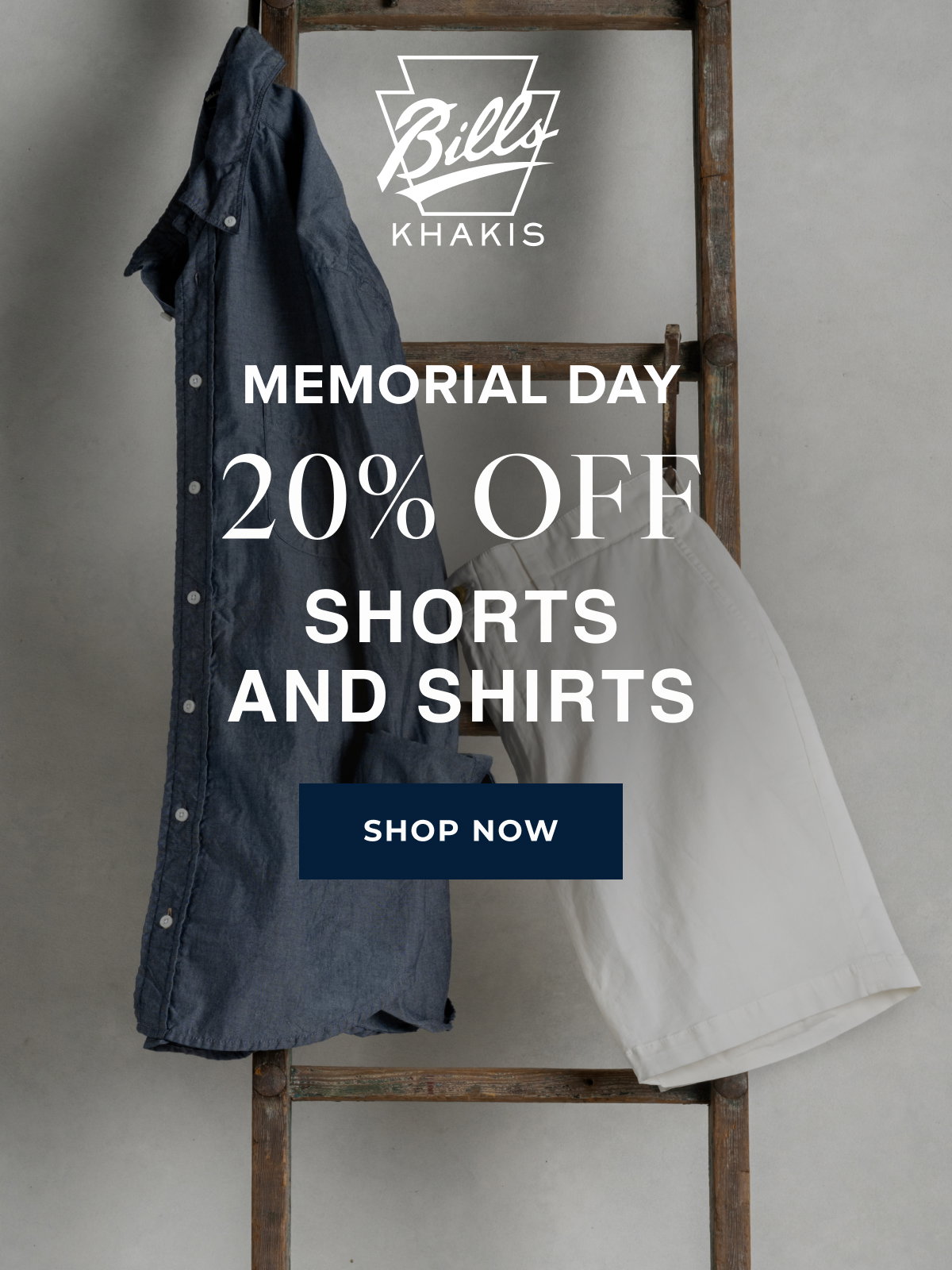 A background photo shows a Bills Khaki shirt and pair of shorts hanging from a vintage wood ladder. The Bills Khakis logo overlays the photo with text that reads: Memorial Day | 20% Off | Shorts and Shirts | Shop Now