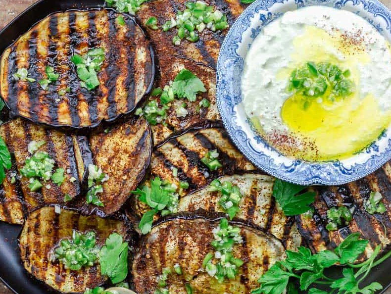 Grilled eggplant with a bowl a tzatziki sauce on a platter.