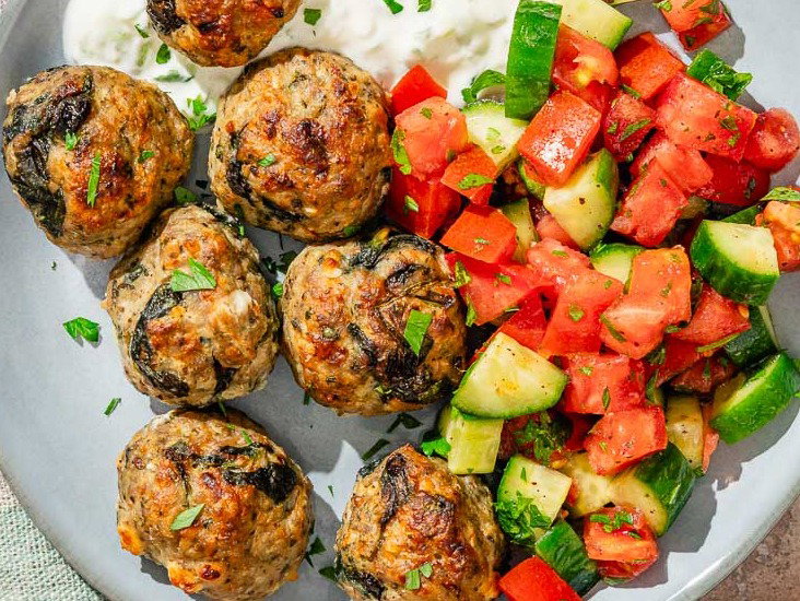 Turkey meatballs on a plate with a Mediterranean tomato and cucumber salad.