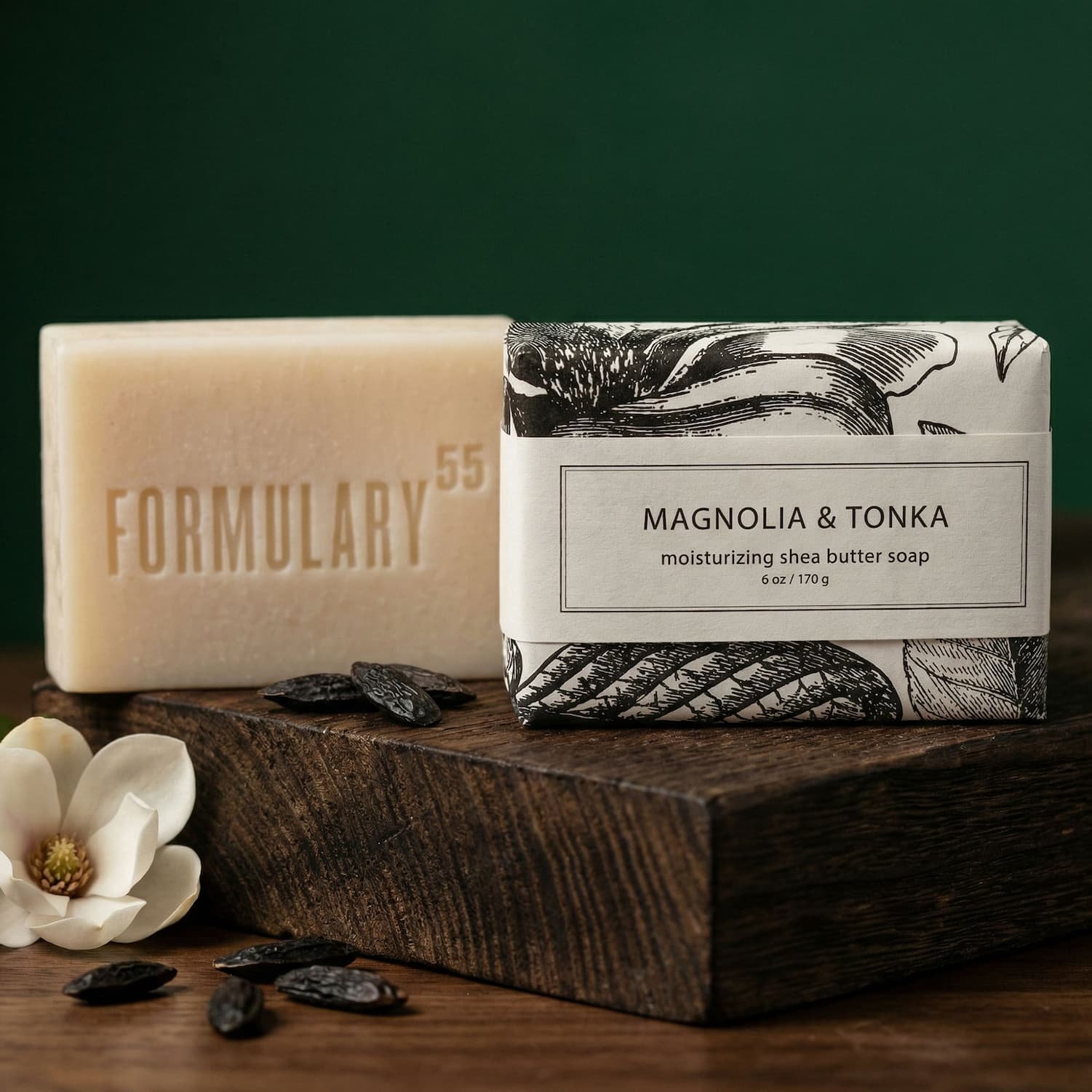 Magnolia & Tonka wrapped shea butter soap sitting on a wood block against a deep rich green background