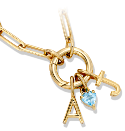 Gold charm necklace with paperclip chain, letter A, cross charm, and blue heart-shaped gemstone pendant.