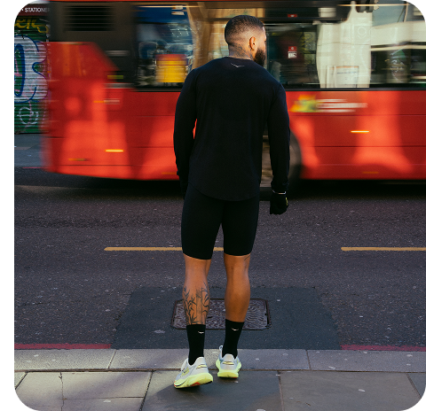 Runner facing a road with a red bus.