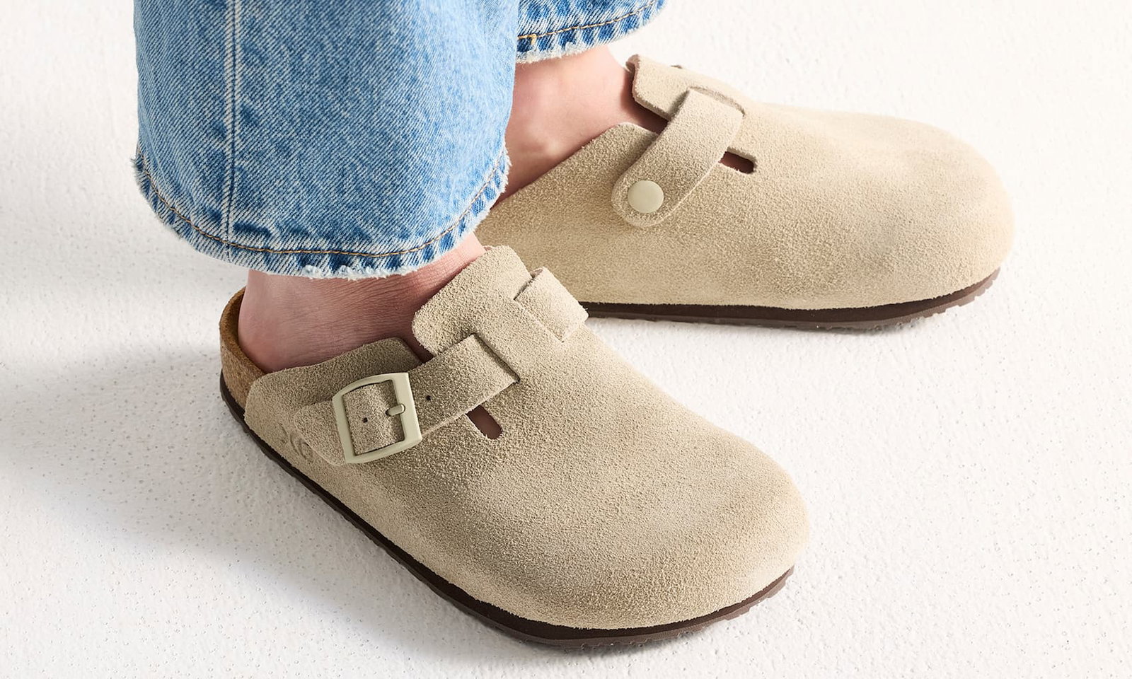 Person som bär sandal med sluten tå i mjuk sandfärg och brun sula