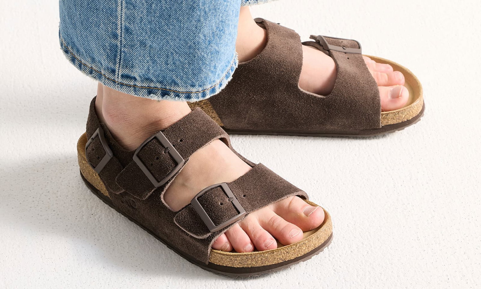 Person som bär bruna sandaler i mocka med rem runt hälen