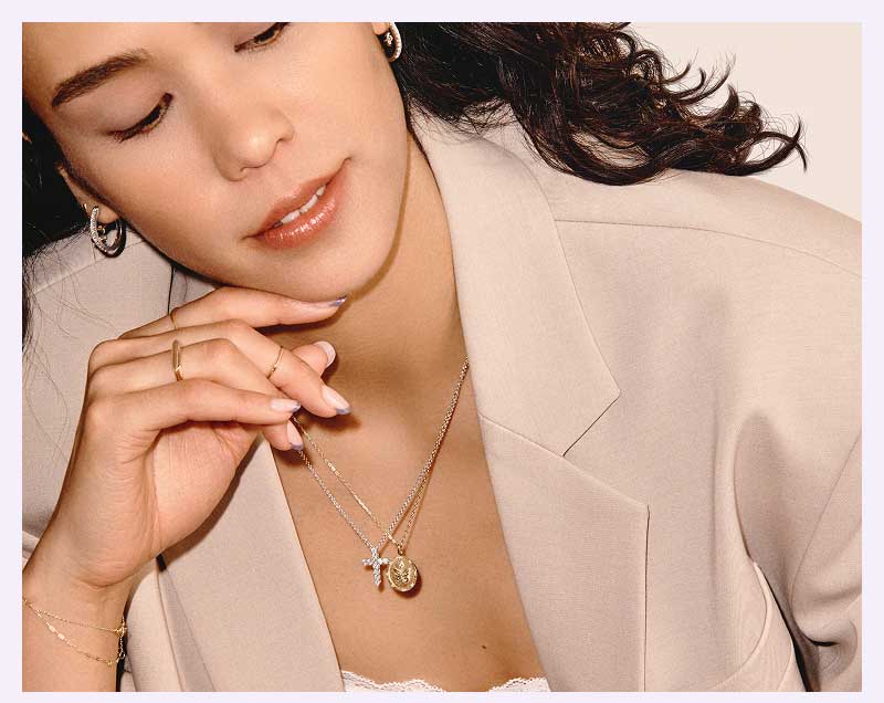 Model layered in silver-set diamond cross pendant necklace & gold-set butterfly medallion pendant necklace.
