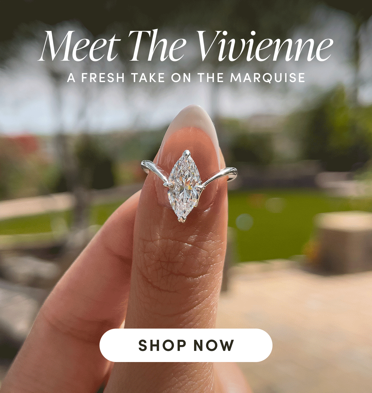 A hand holding a marquise-cut diamond ring outdoors.