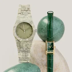 Deux montres-bracelets, l'une avec un bracelet en cuir vert et un cadran rectangulaire, l'autre avec un bracelet à motif camouflage et un cadran rond, exposées sur des pierres.