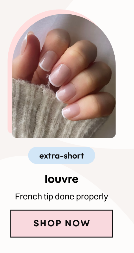 Hand in gray sweater showing short nude press-on nails with clean white French tips