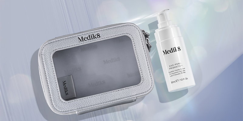 An aesthetic promotional image featuring a white pump bottle of NEW Exo-PDRN Prismatic+ serum next to a small, grey limited-edition beauty bag. The items are set against a soft, light blue background with glowing highlights.