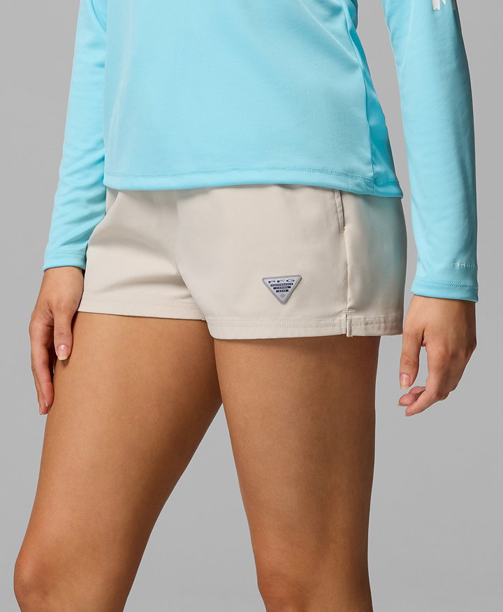 Waist-down image of a woman wearing a blue long sleeve shirt and tan water shorts.