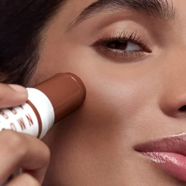 Close-up of a woman's face with Skin-Enhancer Multi-Stick being applied onto her cheek.