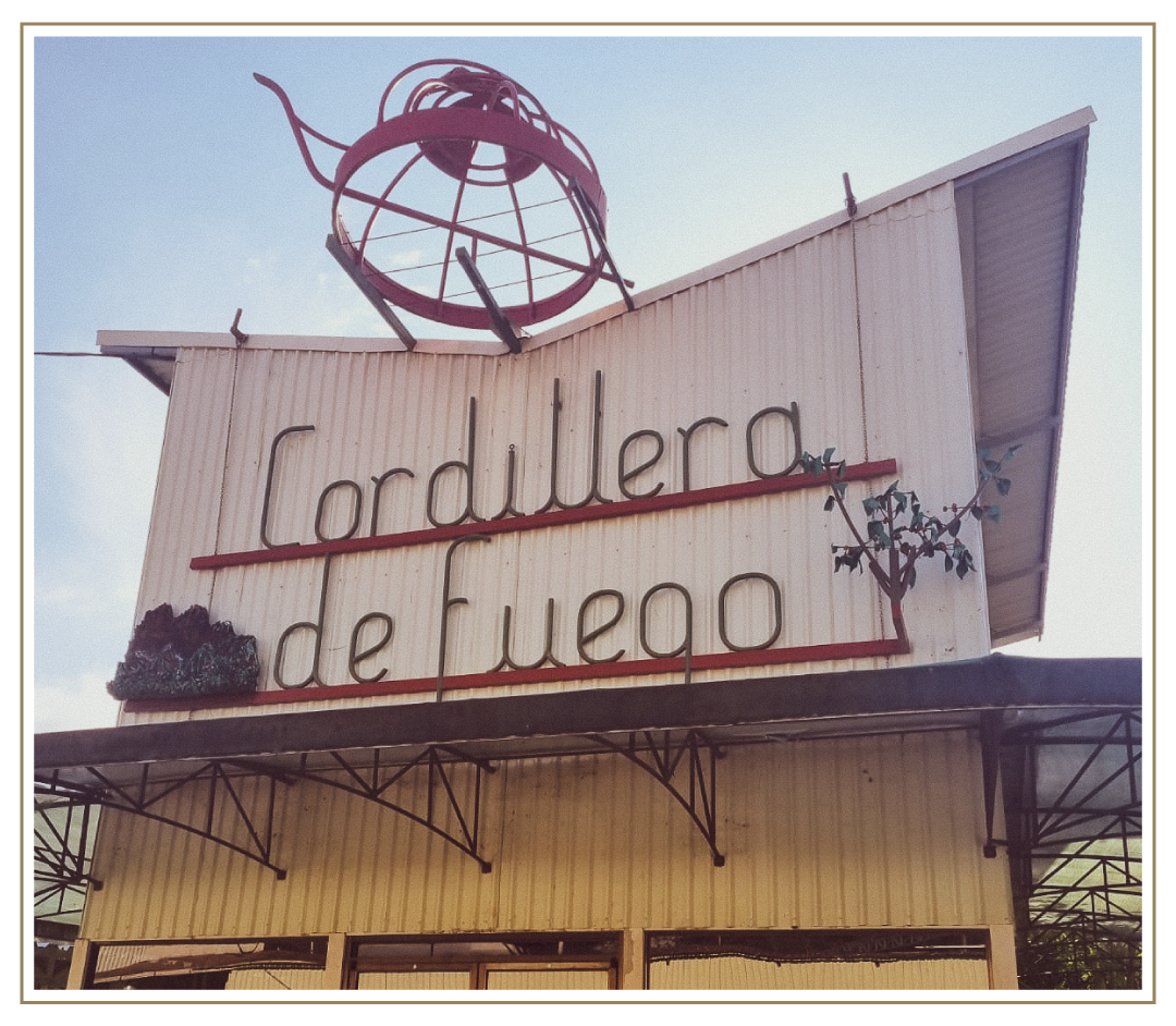 Exterior view of the Cordillera de Fuego coffee mill facility in Costa Rica, featuring a large retro-style sign mounted on the building with sculptural metal artwork above it.