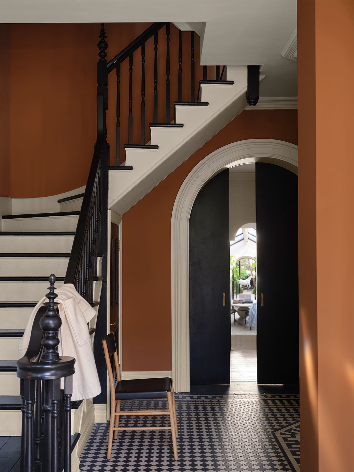 Warm terracotta hallway with black staircase, patterned floor tiles and arched doorway leading to a bright room.