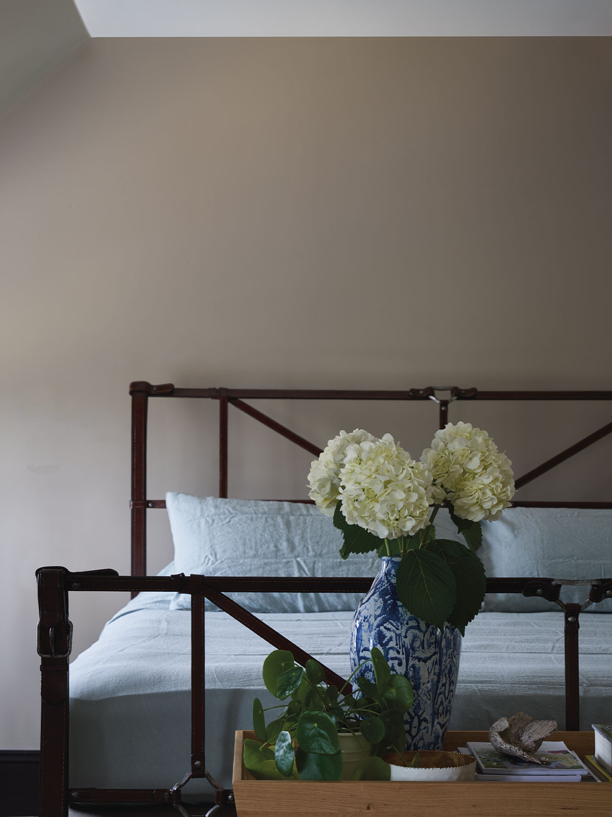 Bed with light blue linen and a vase of white hydrangeas on a wooden tray.