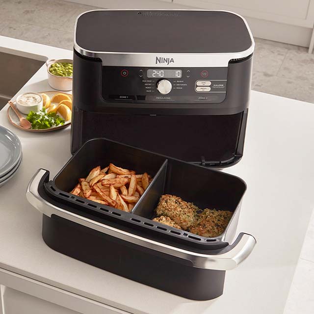 A dual-compartment Ninja air fryer on a kitchen counter, cooking fries and chicken.