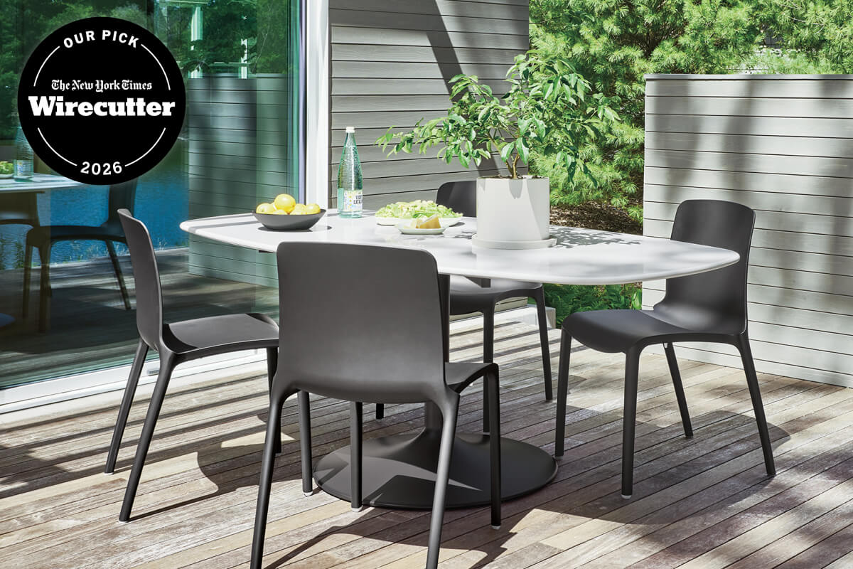 Black outdoor chairs around a white boat-top Aria dining table on a wood deck with Wirecutter award badge.