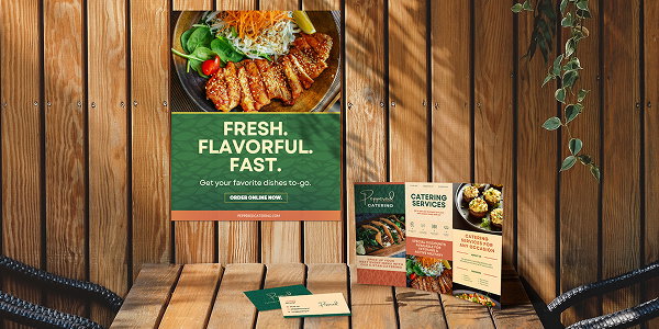 A restaurant table features a branded tri-fold and matching business cards set in front of a promotional poster on a wood-paneled wall.