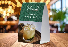 A Peppered table tent sits on a restaurant table with warm lighting and a blurred dining background.