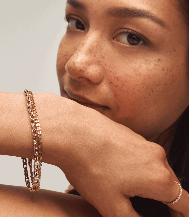 Close-up of a woman wearing two yellow gold chain bracelets and a yellow gold diamond band on her index.
