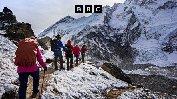 A photograph of a group of climbers on a path on a Himalayan mountain range. A black BBC logo is at the top of the image.