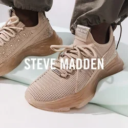 Voeten met lichtbruine gebreide sneakers met dikke zolen, staand op een wit sculpturaal object tegen een effen achtergrond.