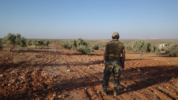 The backside of a senior Uyghur militant stands in an olive grove in northern Syria.