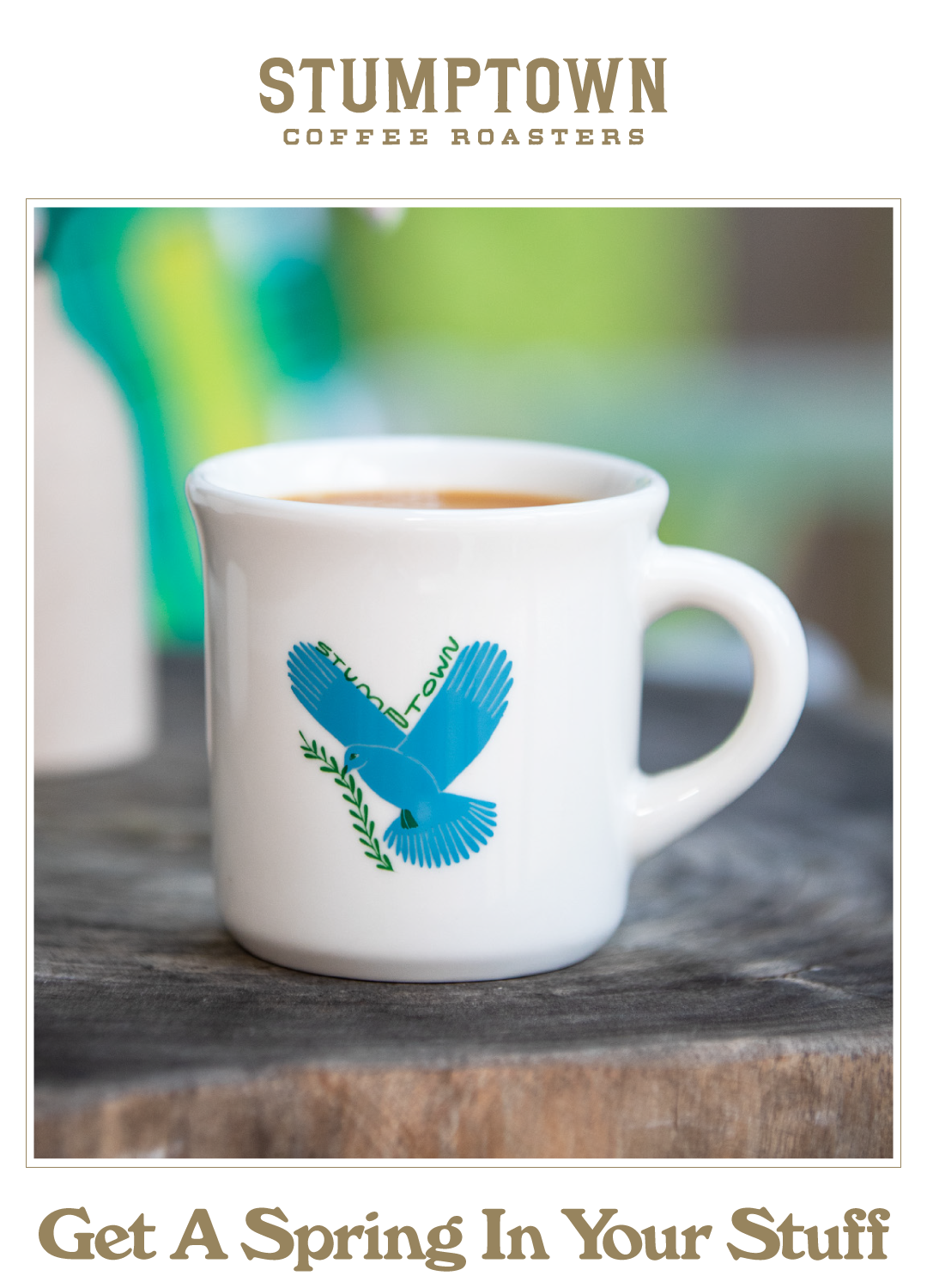 White Stumptown espresso mug with a blue dove illustration sitting on a wooden table. Headline reads: “Get A Spring In Your Stuff.”
