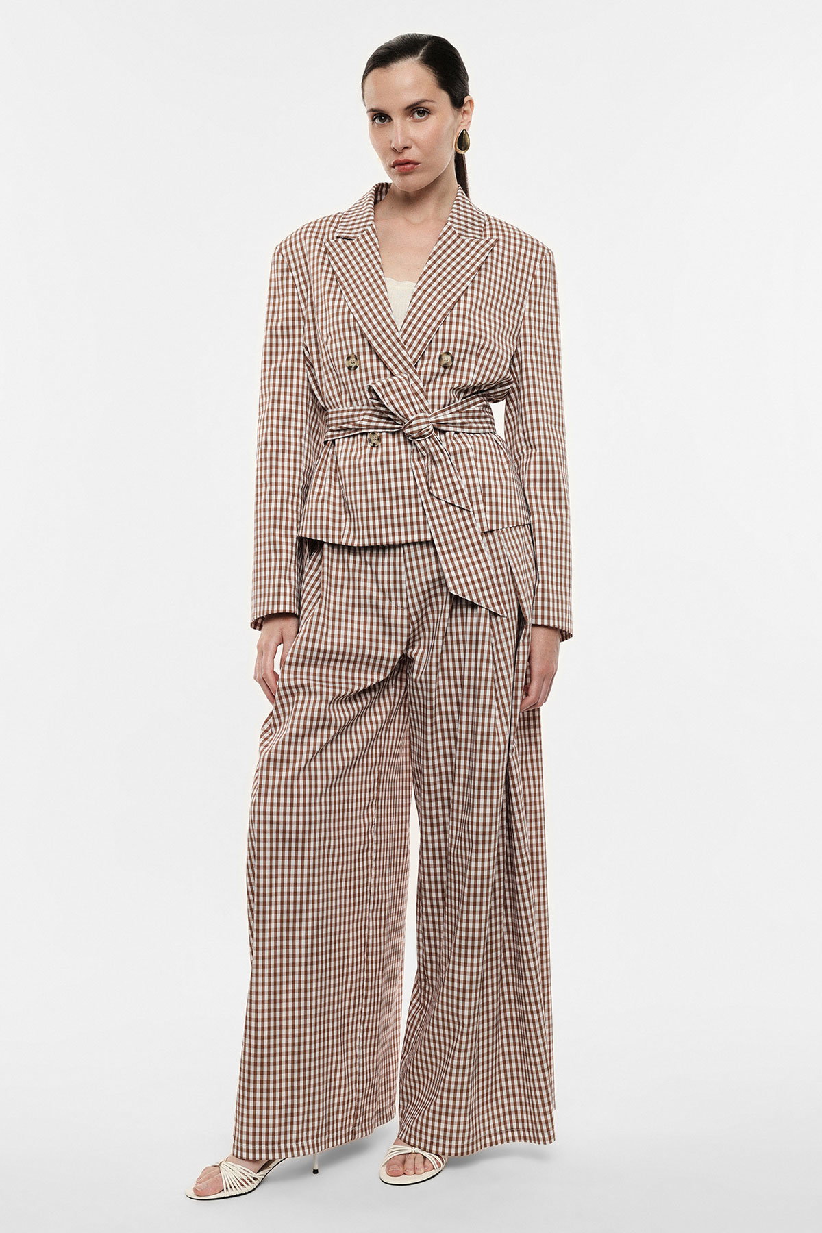 Model wearing brown gingham belted double-breasted blazer and wide-leg trousers with white camisole, gold hoop earrings and sandals