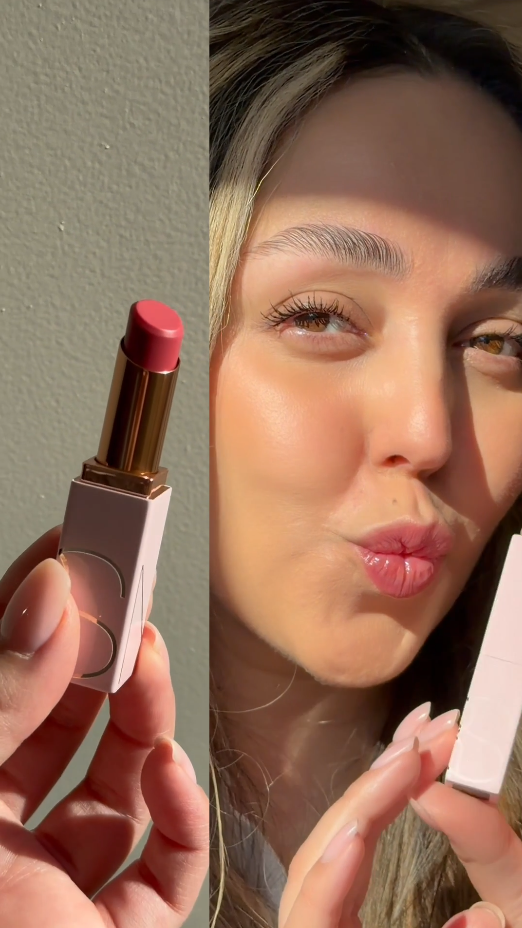 Een vrouw houdt een roze lipstick van NARS vast met gouden details, klaar om haar lippen een subtiele kleur te geven.