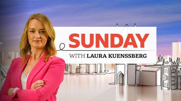 Laura Kuenssberg has long blonde hair and is wearing a pink jacket over a white vest top. She has her arms crossed and is looking at the camera. She is standing on the left and the rest of the image is a cartoon drawing of London. In the centre of the image is a white box with says “Sunday” in red capital letters and then underneath that it says “with Laura Kuenssberg” in black.