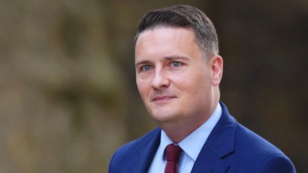 A head-and-shoulders shot of Wes Streeting, who has short brown hair, wears a dark blue blazer, light blue shirt and dark red tie.