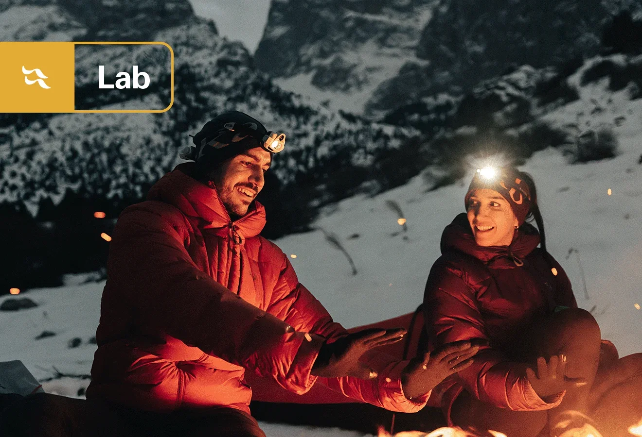 Two alpinist donning a synthetic jackets on a snowy mountainside.