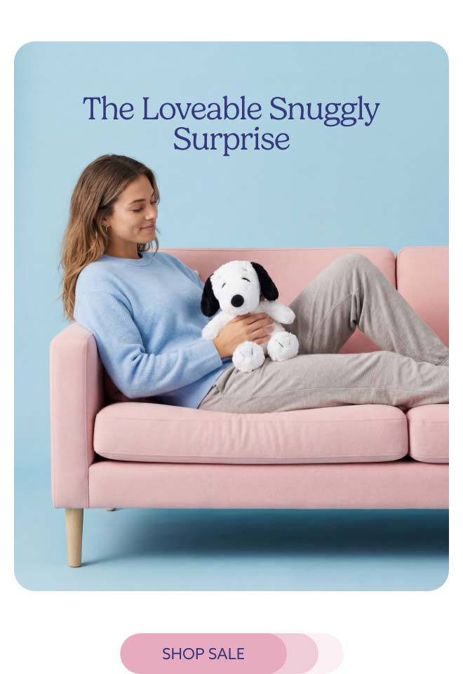 A woman relaxing on a couch with Snoopy Warmies. Shop Sale.