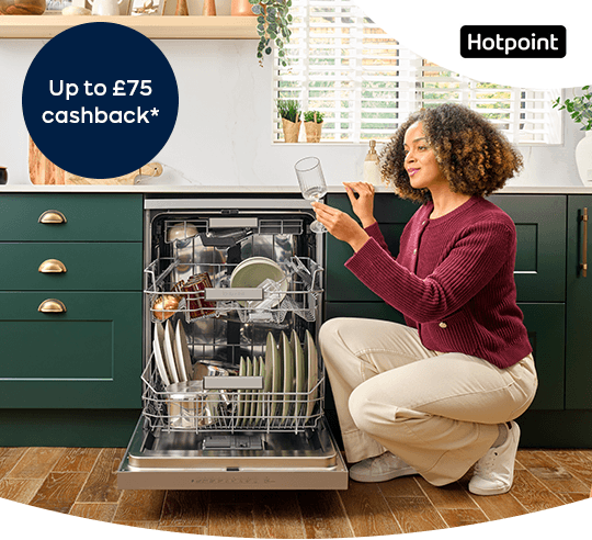 A woman holding a glass beside an open dishwasher.