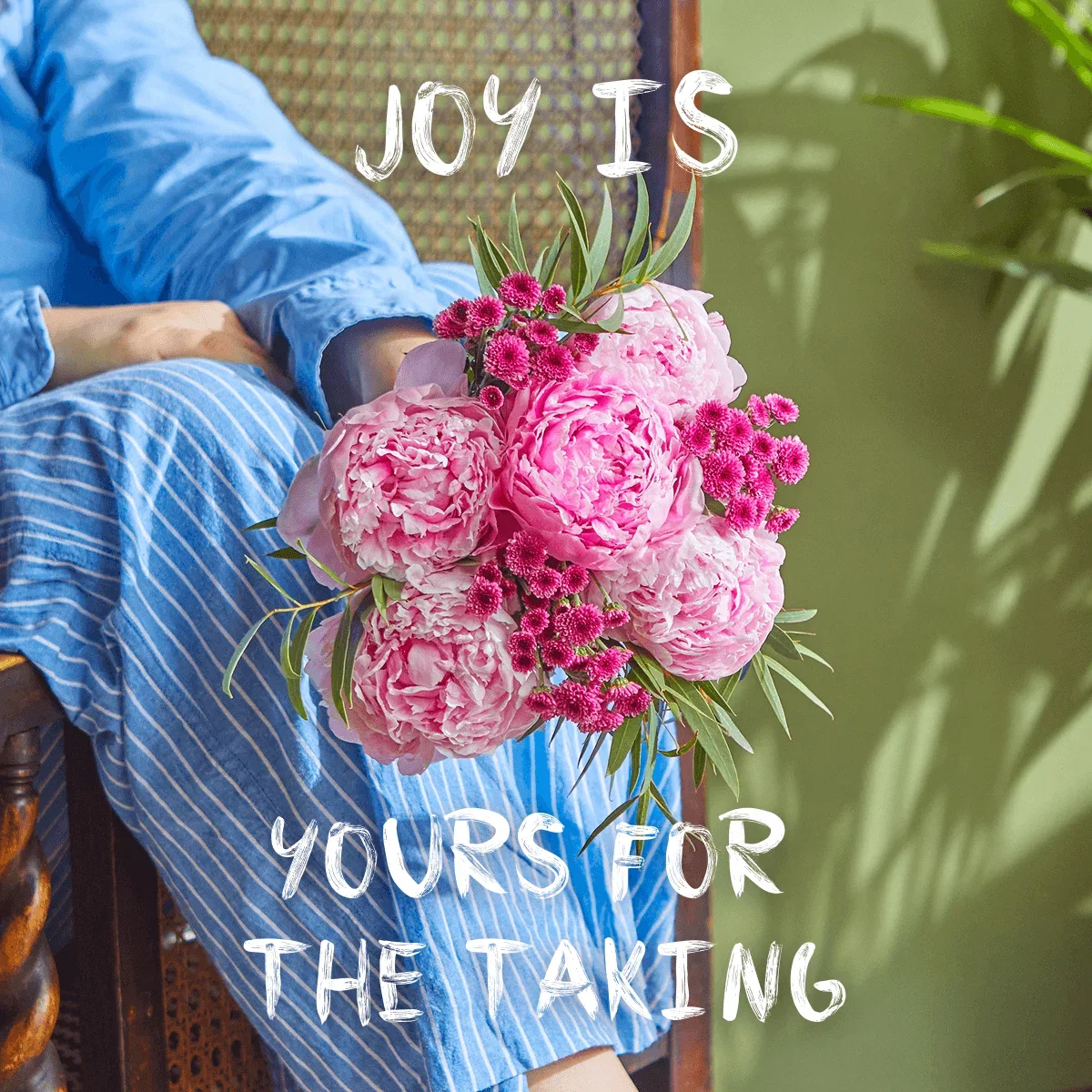 A person in blue striped pyjamas holds a lush bouquet of pillowy pink peonies and vibrant magenta chrysanthemums. White brush-stroke text reads, 