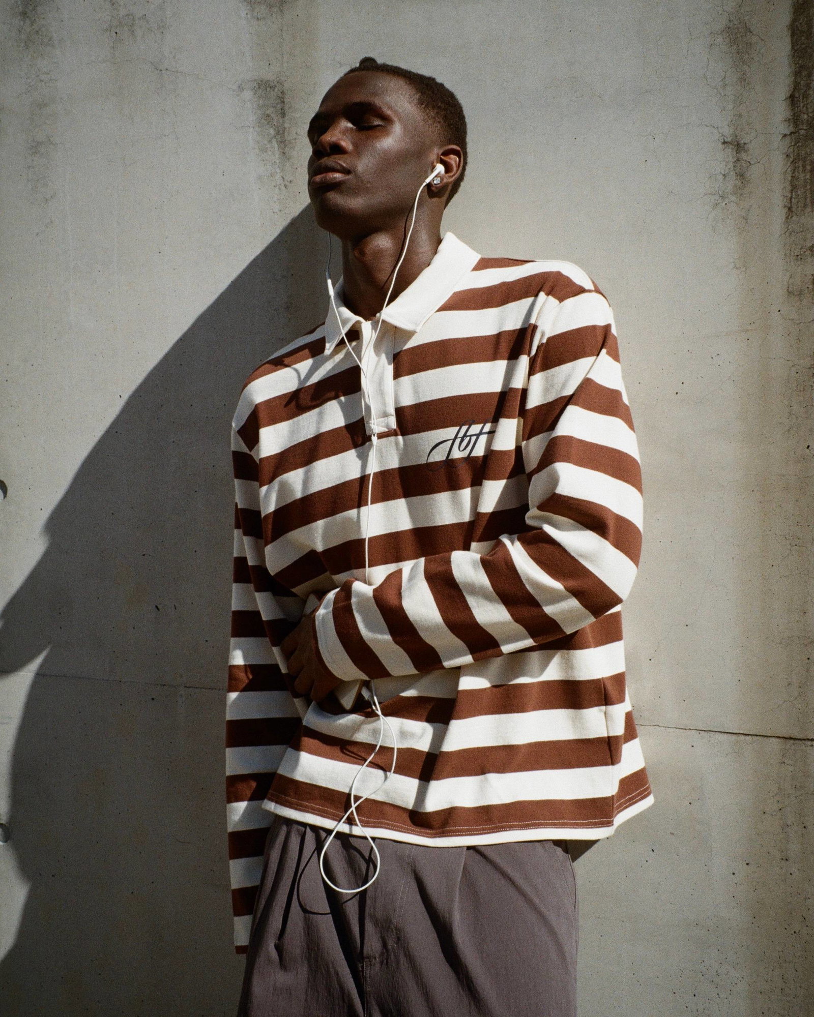 A medium shot captures a person with closed eyes wearing a brown and white horizontally striped long-sleeved polo shirt with a small black embroidered...