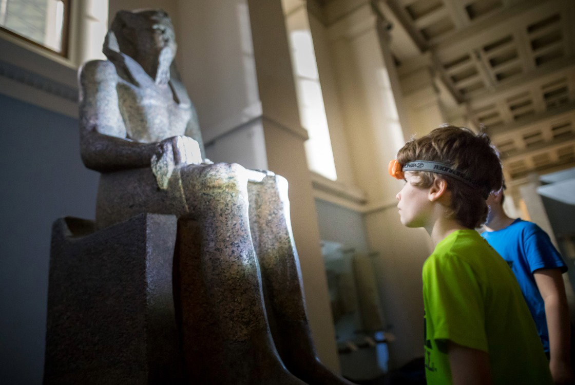 A child wearing a headtorch looking at a statue in the Egypt gallery at a British Museum sleepover.