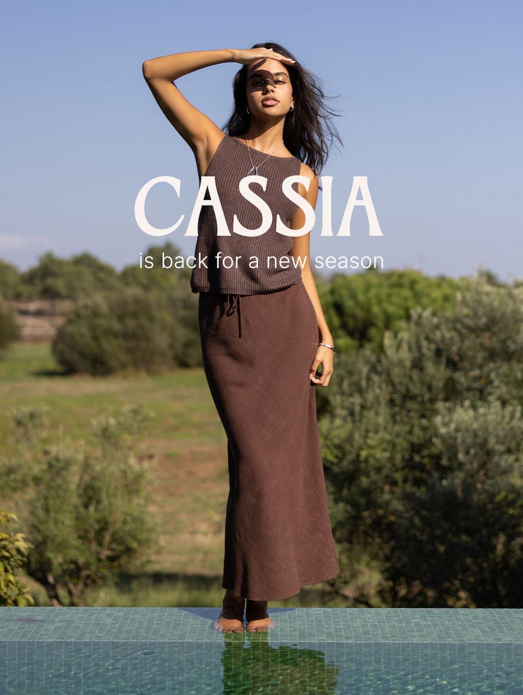 Model standing outdoors in a brown sleeveless knit top and matching maxi skirt beside a pool, with overlay text announcing the return of the Cassia collection for a new season.
