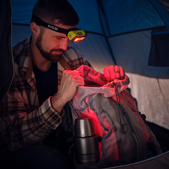 Man using headlamp red lighting mode to look into backpack in a tent. 