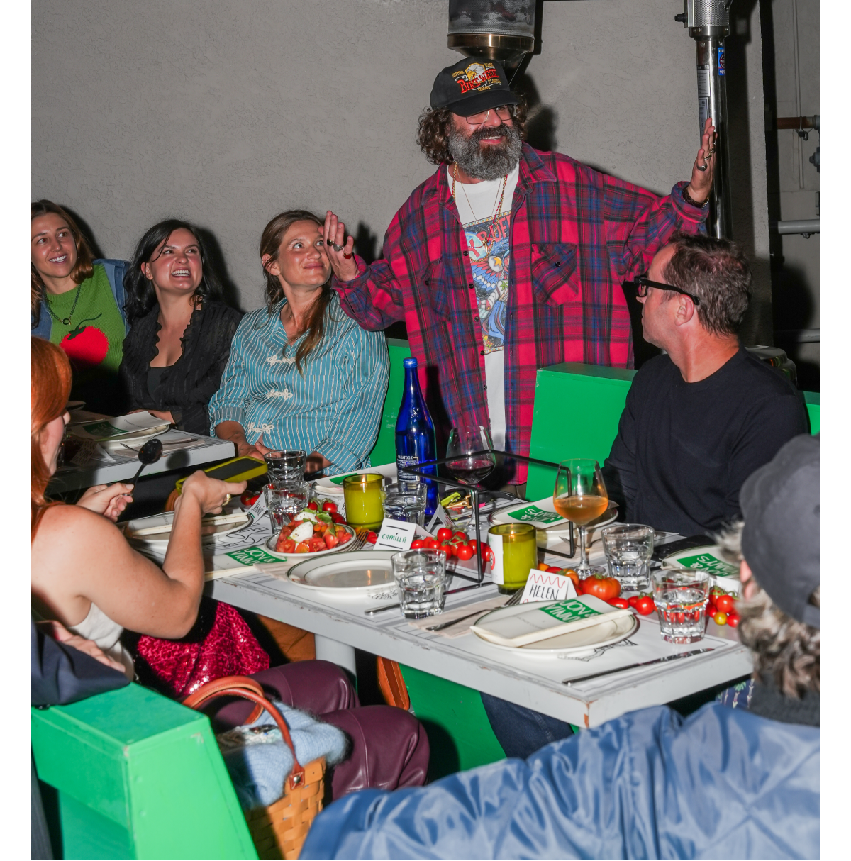 Attendees seated around a candlelit dinner table decorated with cherry tomatoes, wine glasses, and Jon & Vinny’s branded menus.