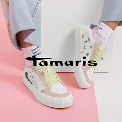 Personne portant un jean en denim clair, des baskets blanches avec des lacets vert pastel et des motifs de style manuscrit, ainsi que des chaussettes blanches avec un texte rouge.