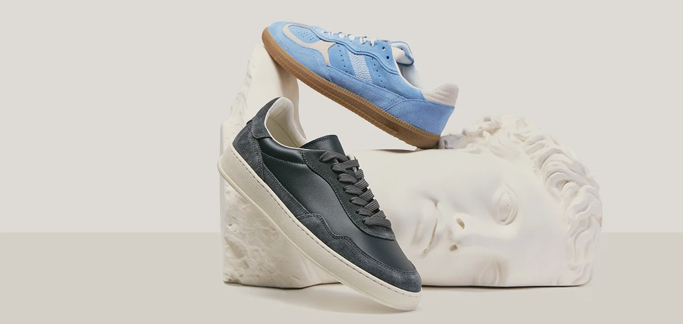 Deux baskets, une noire et une bleue, présentées sur et au-dessus d'une tête de sculpture classique blanche sur un fond neutre.