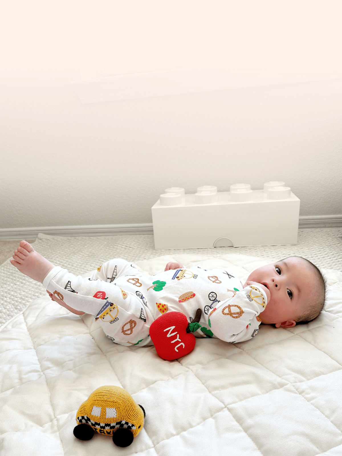 Baby wearing NYC Print Romper playing with organic taxi rattle — lifestyle hero image