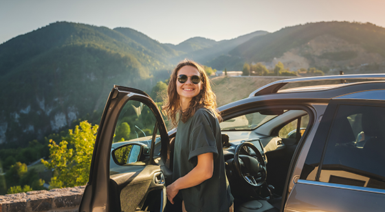 Frau mit Sonnenbrille steigt lächelnd aus dem Mietwagen