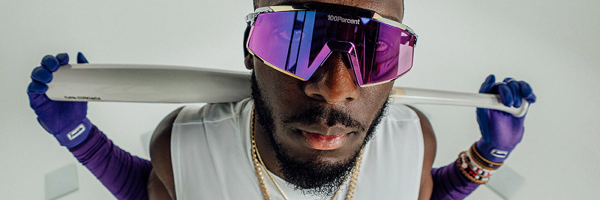 Baseball player Elly De La Cruz wearing 100% Aerocraft® sunglasses in purple mirror lens, holding a bat over his shoulder