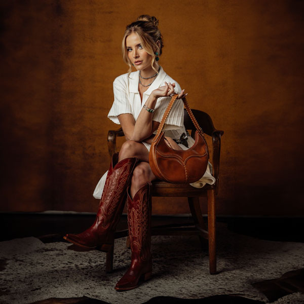 Woman sitting on a wooden chair holding a Tony Lama bag.